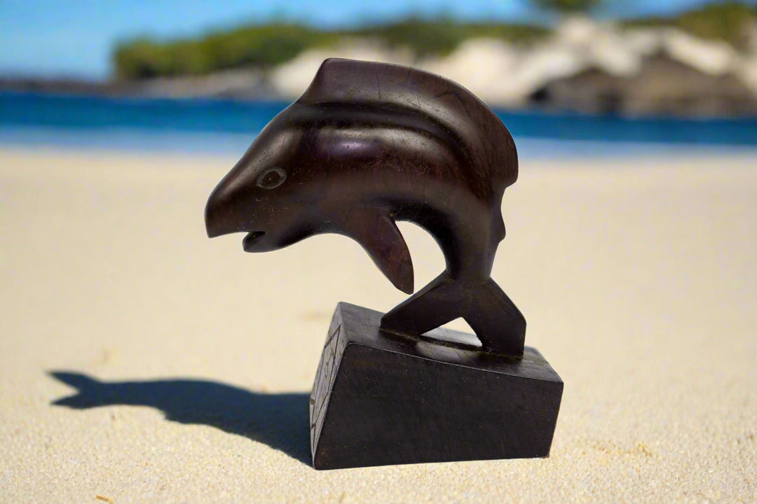 Hand carved cocobolo wood home decor sculpture in the shape of a dolphin, placed on a black base.