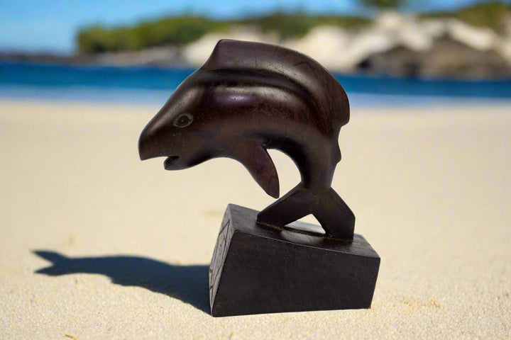 Hand carved cocobolo wood home decor sculpture in the shape of a dolphin, placed on a black base.