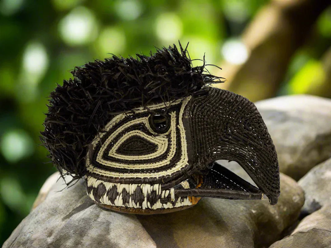 Panama Embera bird mask woven from palm fiber, resting on a rock in a natural outdoor setting.